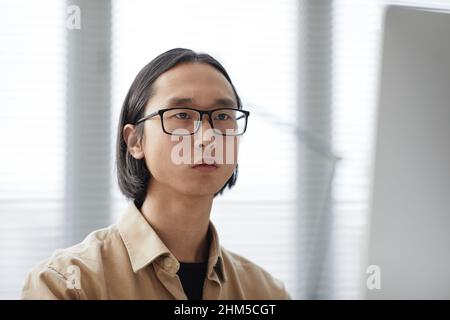 Young contemporary male white collar worker of Asian ethnicity in eyeglasses and casual shirt looking forwards during work Stock Photo