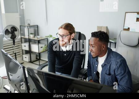 Two young intercultural diversity programmers looking at compute screen while developing new programs in openspace bureau Stock Photo
