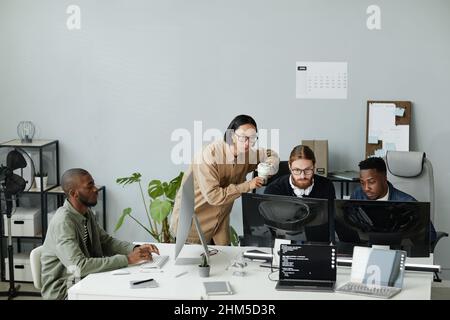 Group of young contemporary program developers gathered in front of computer monitors for discussion of coded data Stock Photo