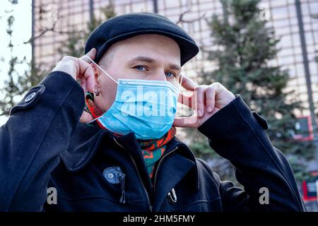 A young man puts on his protective face mask. Outdoors. Coronavirus protection measures. Stock Photo