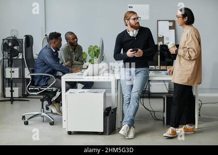 Young contemporary program managers talking at break while their two colleagues working in front of computer in office Stock Photo