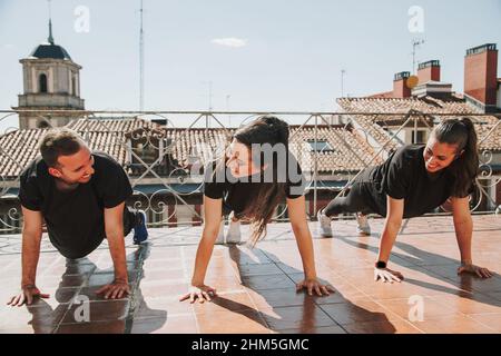 Three people doing push-ups on a rooftop Stock Photo