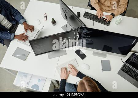 Hands of young intercultural software developers typing on computer keyboards while sitting by desks in office or bureau Stock Photo
