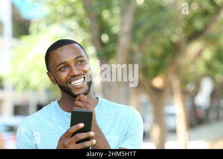 Happy man with black skin thinking holding smart phone in a park Stock Photo