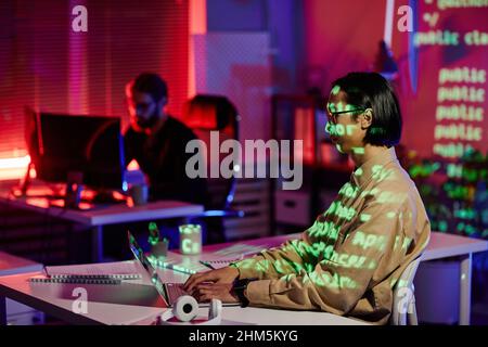 Contemporary young software engineer sitting by workplace in front of laptop in office and working over new program Stock Photo
