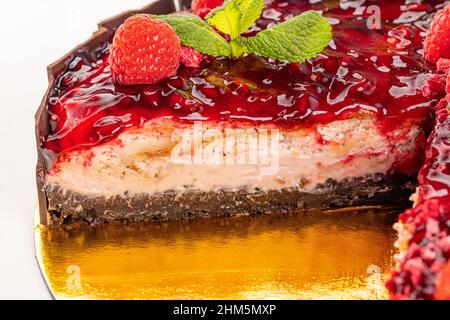 Cheesecake with pomegranate sauce topping decorated with raspberry and mint, close up Stock Photo