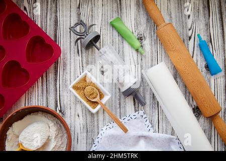 Preparing for baking with kitchenware: heart-shaped silicone mold, rolling pin, confectionery syringe, glaze, flour, sugar on pink background. Valenti Stock Photo