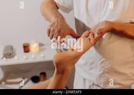 Reflexology foot massage with wooden thai stick. Acupressure in alternative medicine. Oriental physiotherapy through energy points on body. Bodycare and SPA in Thailand. Stock Photo