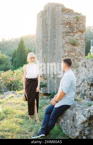 Woman walks towards a man sitting on the ruins of a stone wall Stock Photo