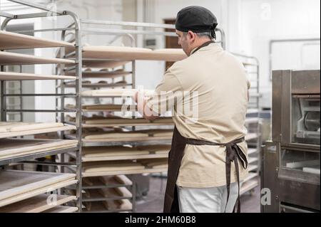 Baker placing tray with formed raw dough on rack trolley ready to bake in the oven. High quality photo Stock Photo