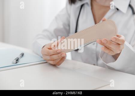 Doctor holding an insole while sitting at a table. Orthopedist tests the medical device. Orthopedic insoles. Foot care. Flat Feet Correction Stock Photo