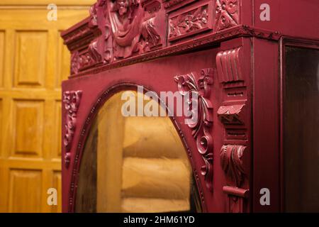 Old retrieved patterned cupboard painted in red color with glass in front with wooden house walls and door in background. Restoration of antique Stock Photo