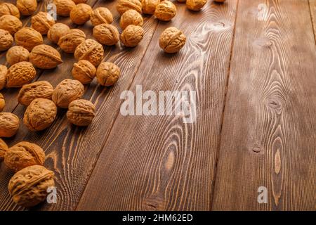 many walnuts with shells randomly scattered on brown wooden surface with copy space at right side of picture Stock Photo