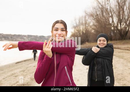 Young female friends stretching their arms before their morning training Stock Photo