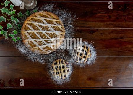 Top view Delicious apple pie large and two small blue berry tarts on wood table background. Stock Photo