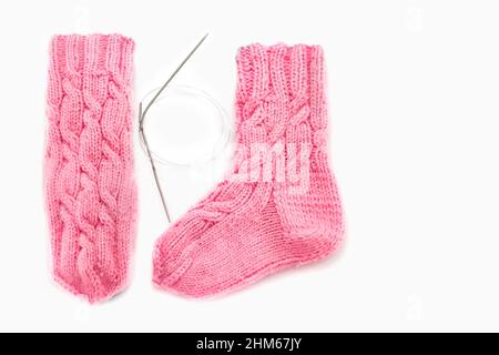 Pink knitted socks with Aran pattern and knitting needles on a white background. Place for text. Warm handmade knitted socks with beautiful patterns. Stock Photo