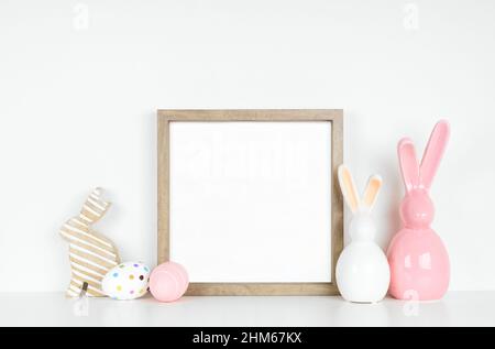 Mock up wood frame with Easter egg and bunny decor on a white shelf. Square frame against a white wall. Copy space. Stock Photo