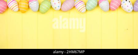 Colorful Easter Egg top border over a soft yellow wood banner background. Overhead view with copy space. Stock Photo