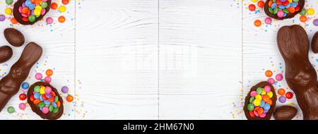 Easter candy, chocolate bunnies and eggs. Top view double border against a white wood banner background. Copy space. Stock Photo