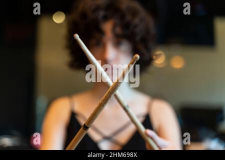 Defocused portrait of a young woman with curly hair playing drums with drumsticks Stock Photo