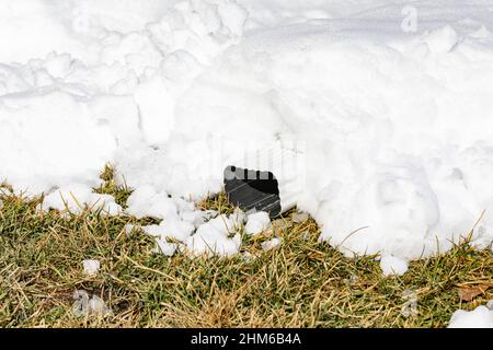 Roof gutter downspout covered in snow after winter storm. Roof damage, gutter maintenance, snow removal, and home repair concept. Stock Photo