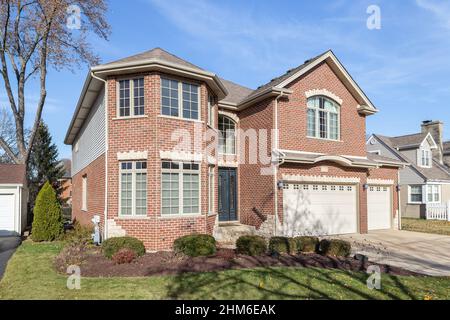 A large, two story red brick home with a three car garage. Stock Photo