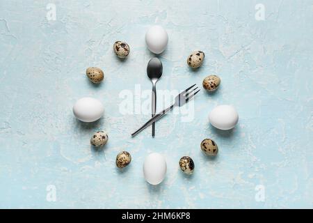 Clock made of eggs and cutlery on color background Stock Photo