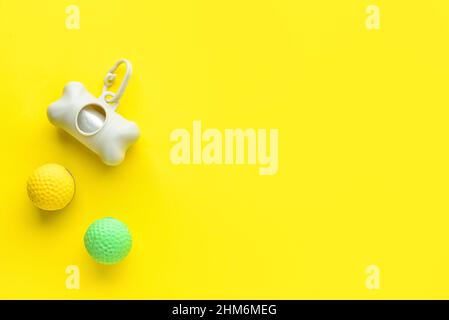 Dispenser with pet waste bags and balls on yellow background Stock Photo