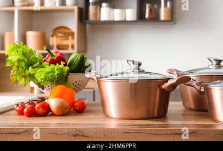 Shiny cooking pot and colander with fresh vegetables on counter in modern kitchen Stock Photo