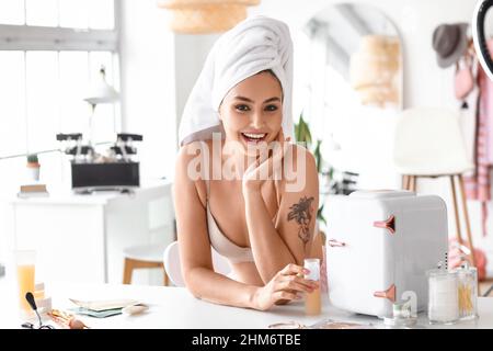 Young woman with makeup product and small cosmetic refrigerator on table in dressing room Stock Photo