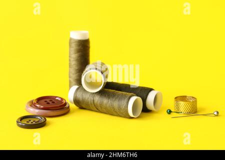 Sewing thread spools, pins, thimble and buttons on color background Stock Photo
