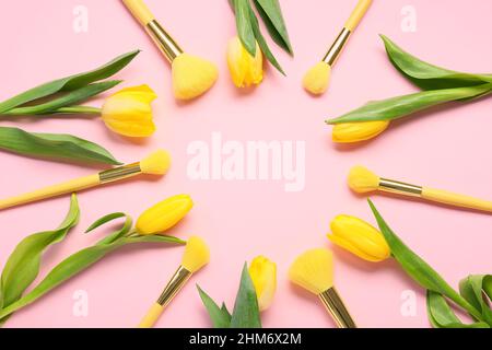 Frame made of makeup brushes and flowers for International Women's Day celebration on pink background Stock Photo