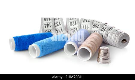 Thread spools, measuring tape and thimble on white background Stock Photo