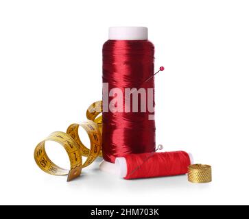 Red thread spools, thimble, measuring tape and ball pins on white background Stock Photo