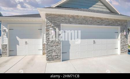 Panorama Puffy clouds at sunset Three-car side hinged garage doors with stone veneer wall siding Stock Photo