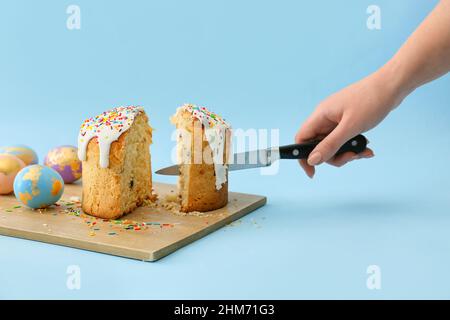 Woman cutting delicious Easter cake on blue background Stock Photo