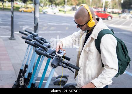 Bald Latin man taking a public scooter with an app on his cell phone Stock Photo