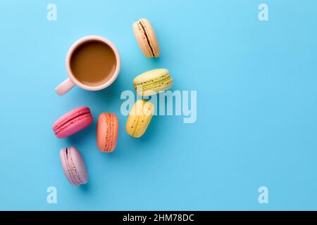 Colorful delicious French dessert macaron or macaroons with a coffee cup on blue background. Top view with copy space. Stock Photo