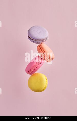 Colorful delicious French dessert macaron or macaroons flying or falling in motion on pink background. Stock Photo