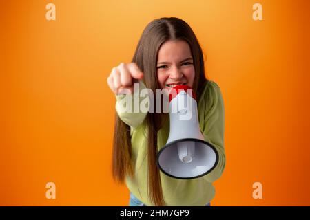 Teen girl making announcement with megaphone against orange background Stock Photo