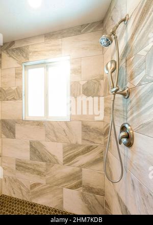 Vertical Sun flare Shower stall interior with marble tile surround and small hexagon pattern tile flooring Stock Photo