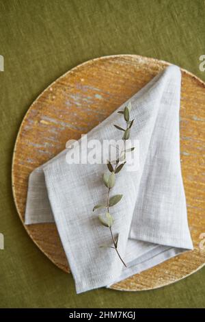 Table setting option. A linen grey napkin is neatly folded on a brown plate. Olive background. Stock Photo