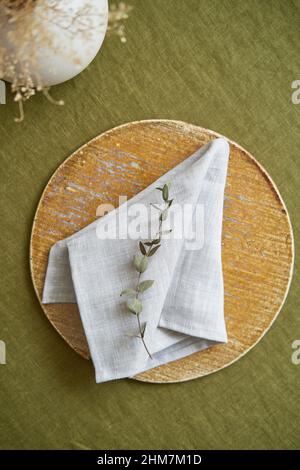 Table setting option. A linen grey napkin is neatly folded on a brown plate. Olive background. Stock Photo