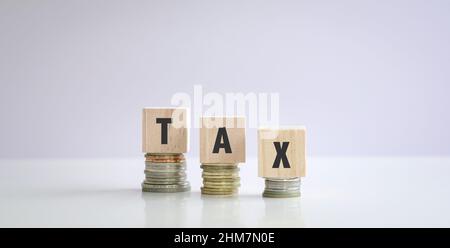 The word Tax on wood cubes, on top of stacked coins. Tax filing concept. Stock Photo