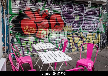 Street art on closed security shutters at cafe in Camden Town London , deserted with no customers, empty chairs. Stock Photo