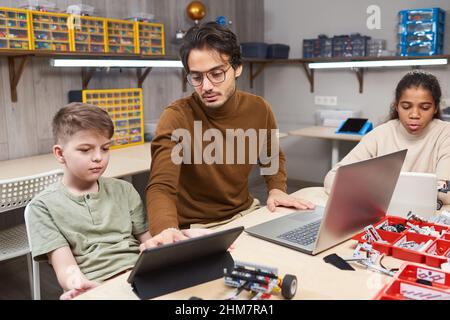 Portrait of young man teaching robotics class to diverse group of children in modern school Stock Photo