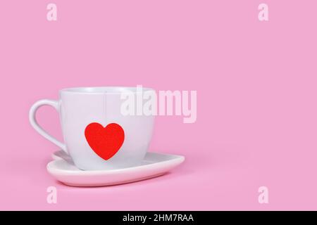 Tea cup with red heart shaped tea bag paper on pink background with copy space Stock Photo