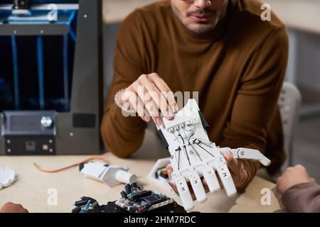 Close up of young man holding robotic hand while demonstrating 3D technology in engineering class, copy space Stock Photo
