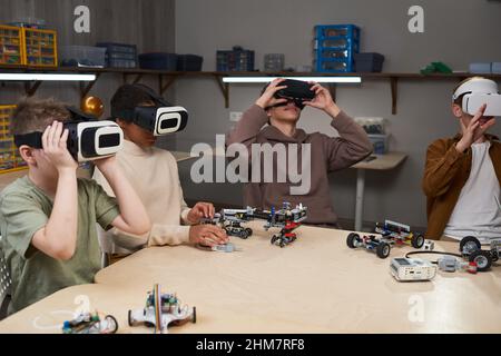Diverse group of children wearing VR gear in school while sitting at table and using augmented reality in innovative robotics class Stock Photo