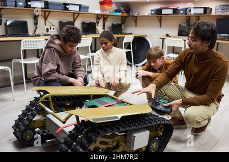 Full length portrait of diverse group of children looking at big crawler robot machine in engineering class at school Stock Photo